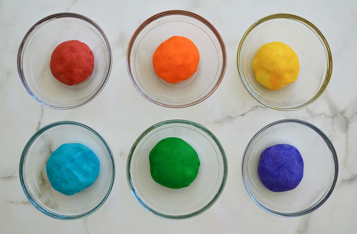 Six glass bowls containing rainbow colors of playdough