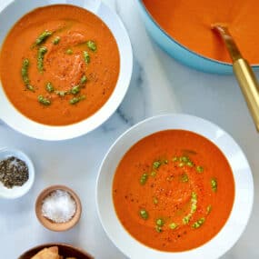 A teal stock pot of tomato soup with two white bowls filled with soup