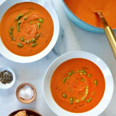A teal stock pot of tomato soup with two white bowls filled with soup