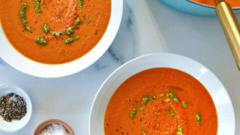 A teal stock pot of tomato soup with two white bowls filled with soup