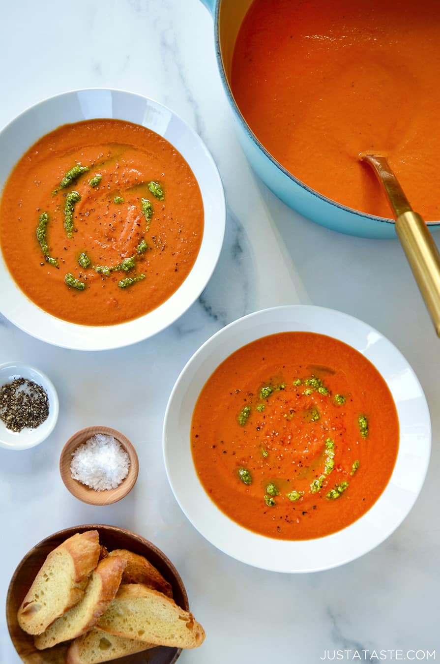 A teal stock pot of tomato soup with two white bowls filled with soup