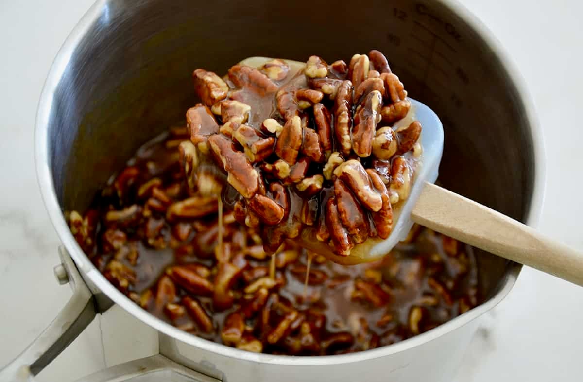 A spatula with pecans over a pot containing pecan filling.