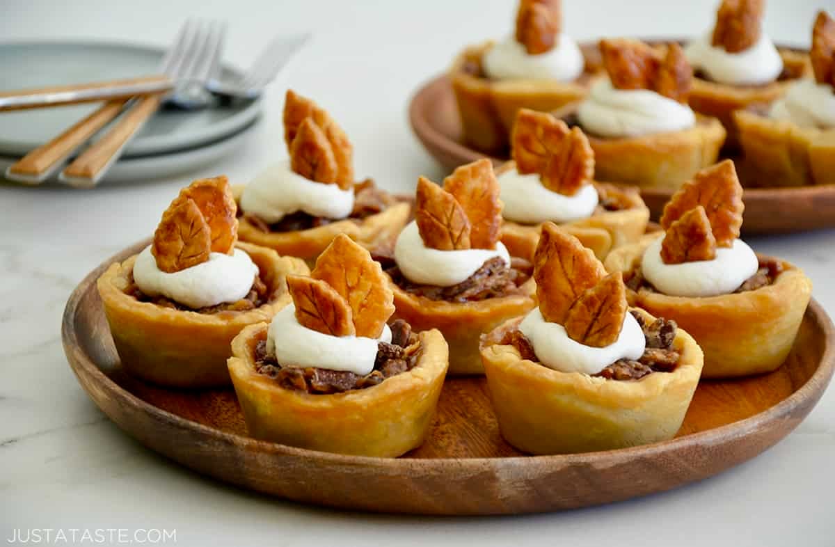 Individual mini pecan pies topped with whipped cream on serving plate.