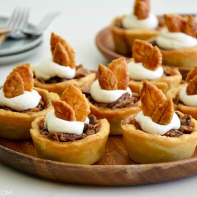 Individual mini pecan pies topped with whipped cream on serving plate