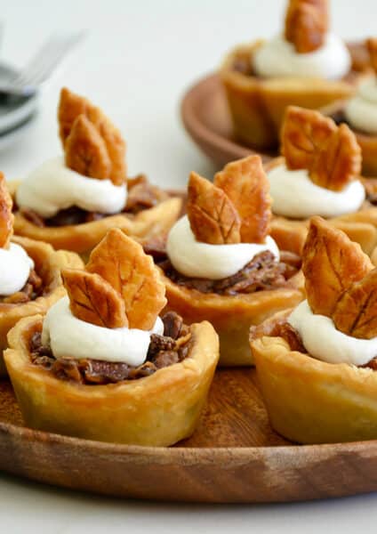 Individual mini pecan pies topped with whipped cream on serving plate