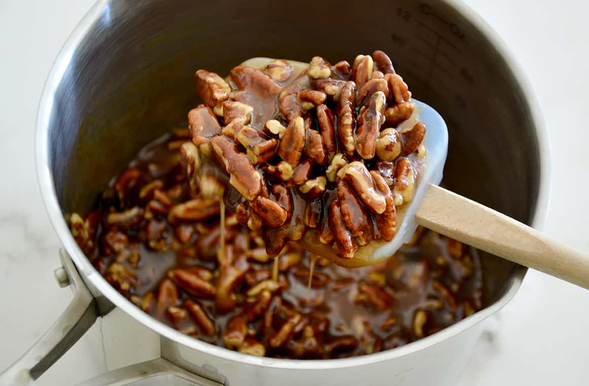 A spatula with pecans over a pot containing pecan filling