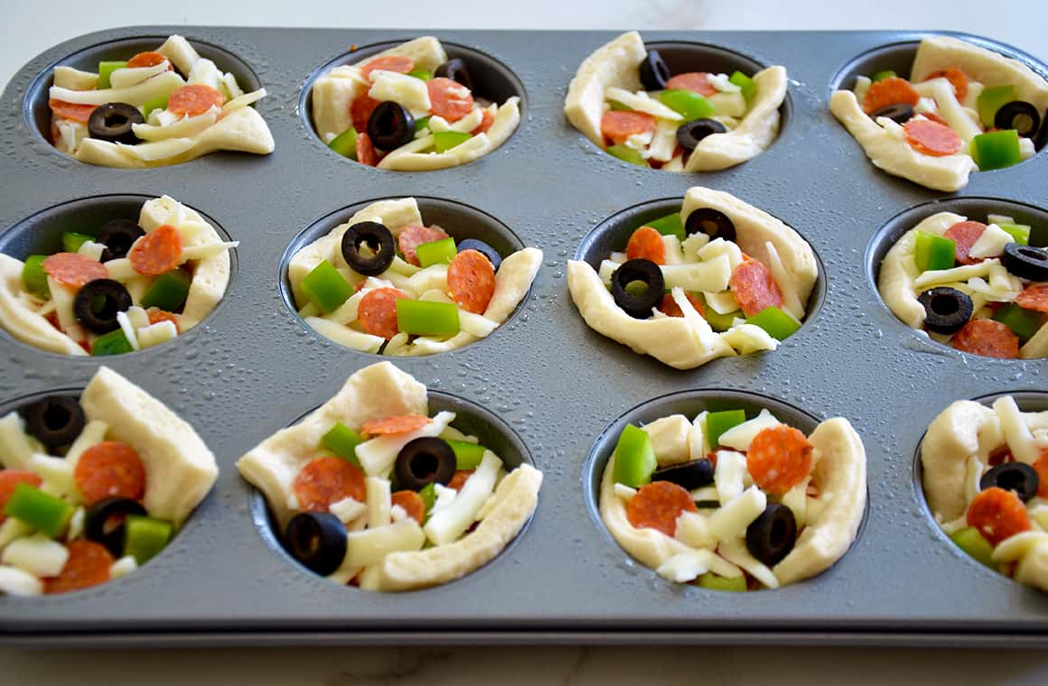 Individual pizzas in a muffin tin with pepperoni, green bell peppers and black olives