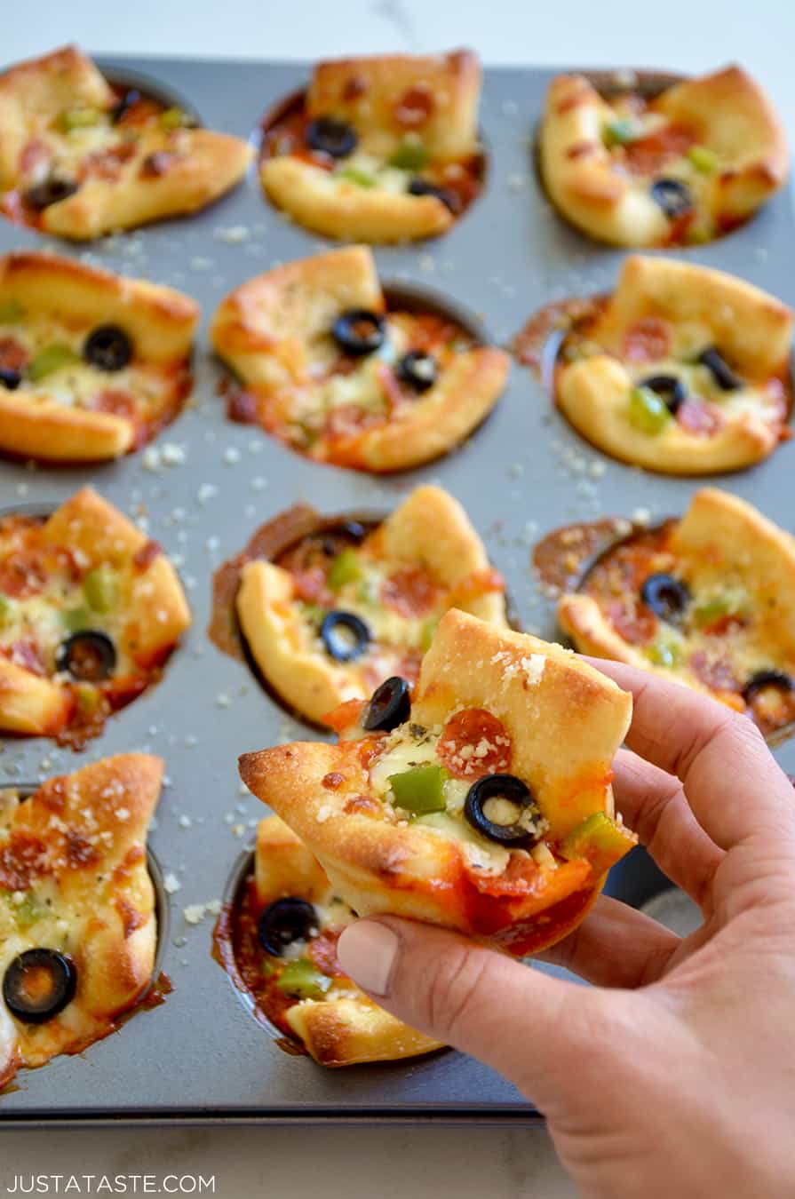 A hand holding an Easy Cheesy Pizza Cup with more in a muffin pan the background