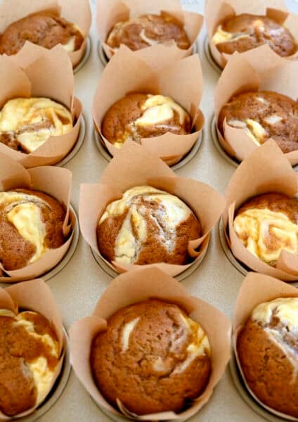 A muffin tin with homemade pumpkin cream cheese muffins in brown and white striped muffin liners.