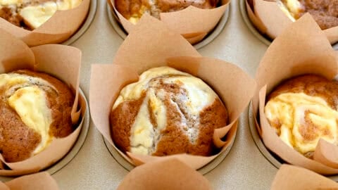 A muffin tin with homemade pumpkin cream cheese muffins in brown and white striped muffin liners.