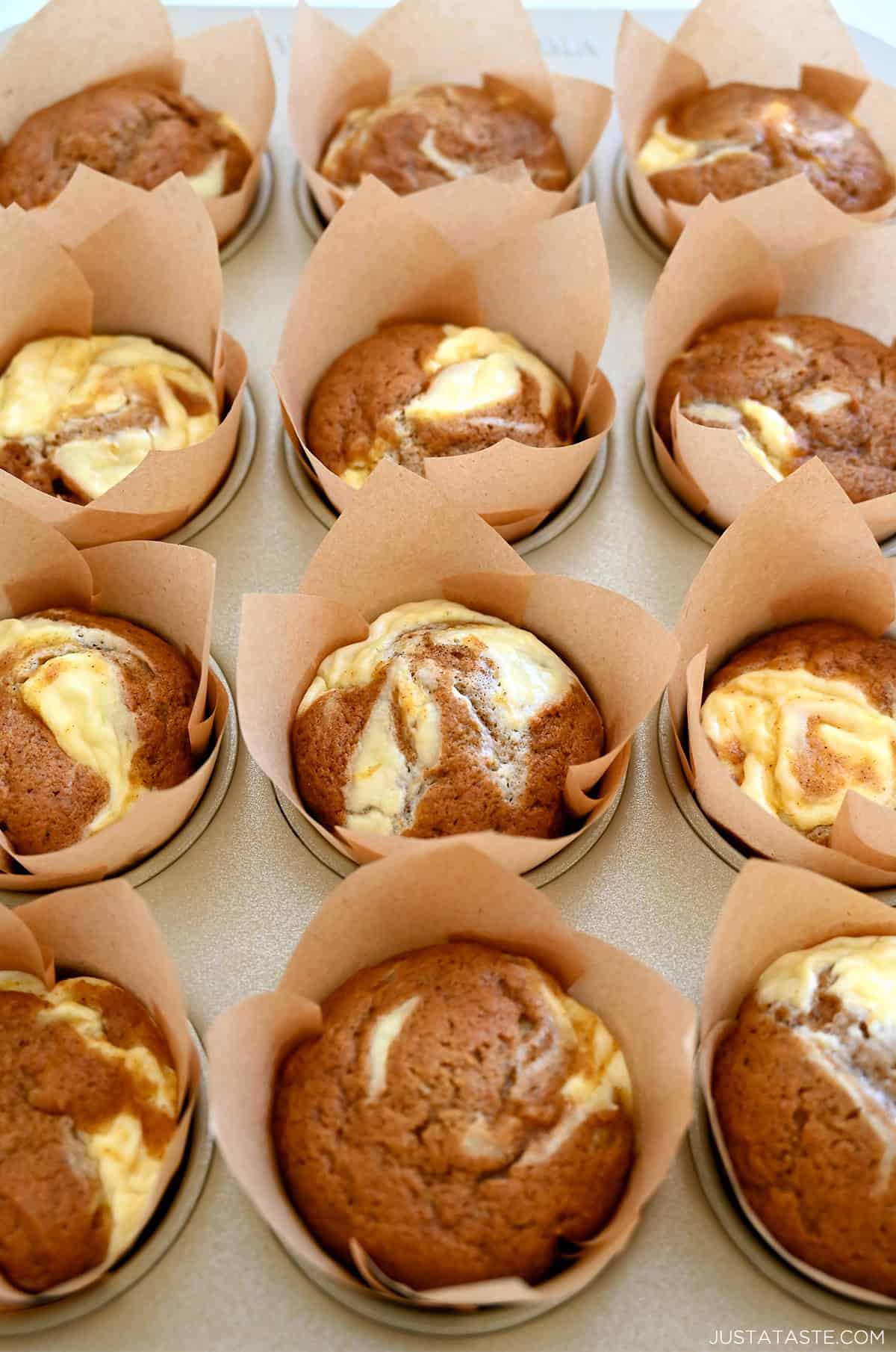 A muffin tin with homemade pumpkin cream cheese muffins in brown and white striped muffin liners.