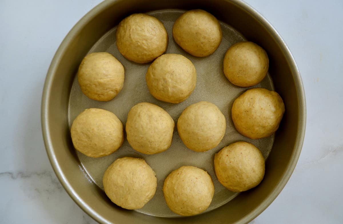 Circles of bread dough in a gold baking pan.