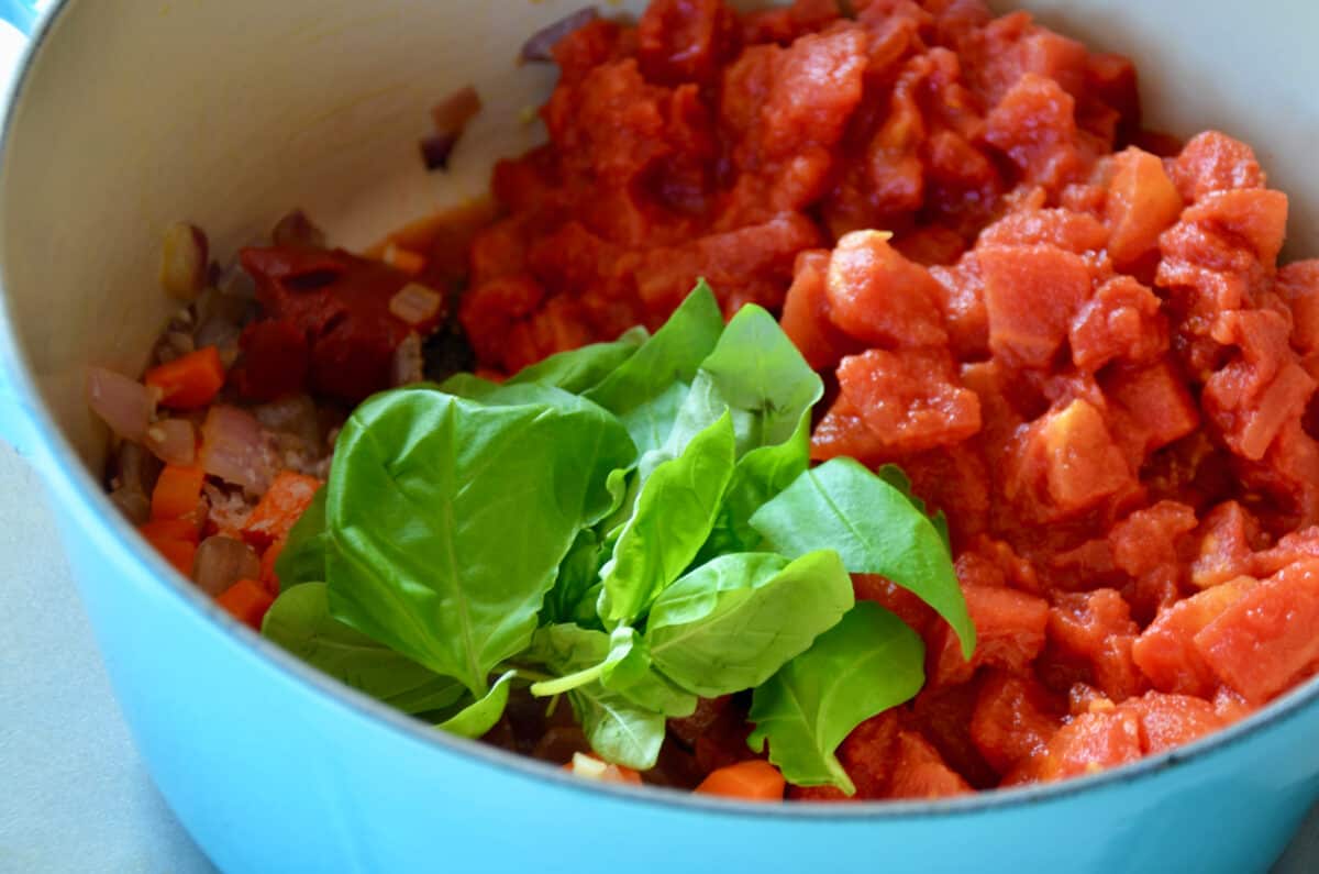A teal pot containing tomatoes and fresh basil