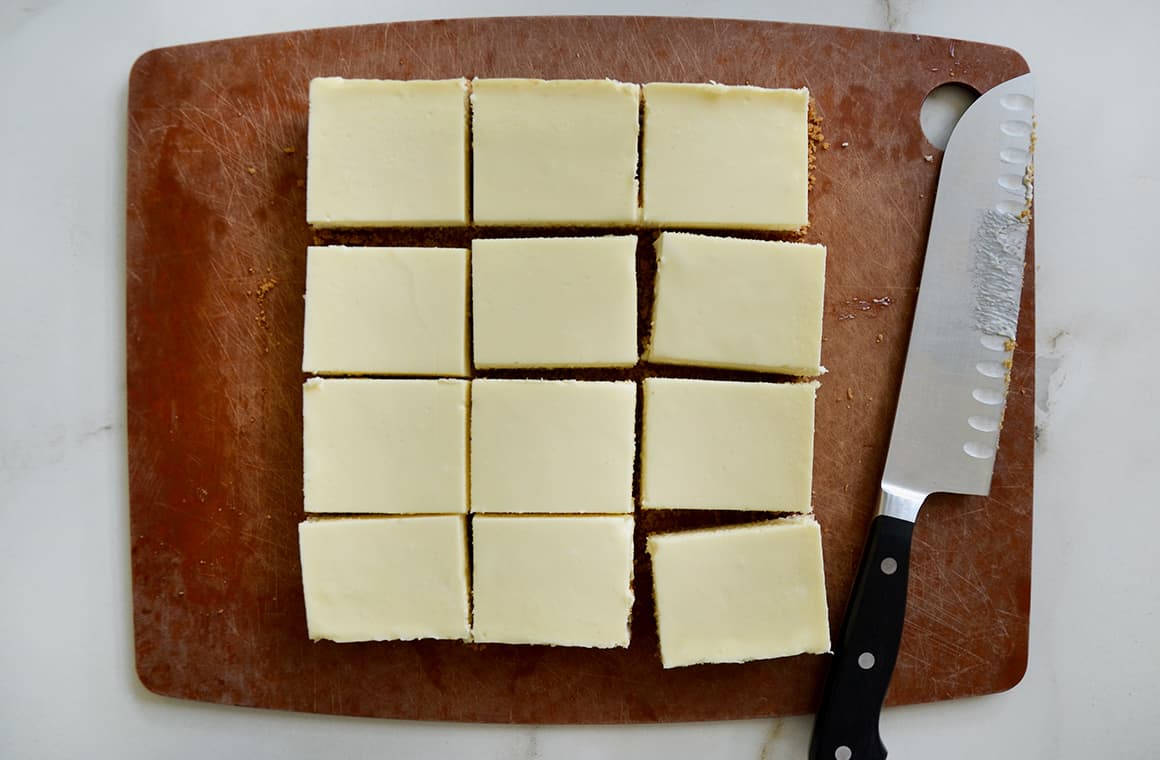 Sliced cheesecake bars next to a sharp knife on a wooden cutting board