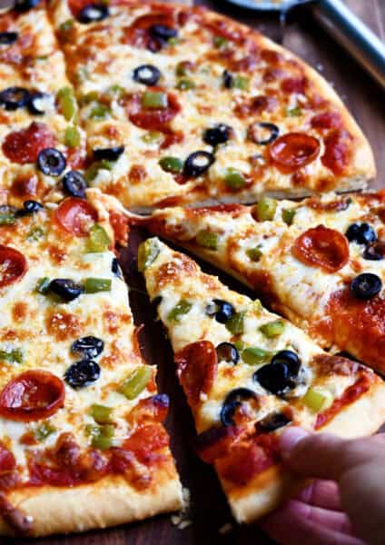 Freshly baked homemade pizza dough without yeast topped with melty cheese, mini pepperoni, sliced green peppers and black olives.