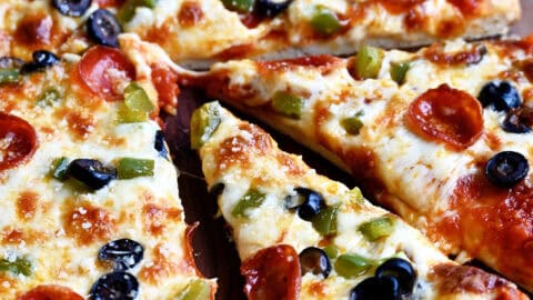 Freshly baked homemade pizza dough without yeast topped with melty cheese, mini pepperoni, sliced green peppers and black olives.