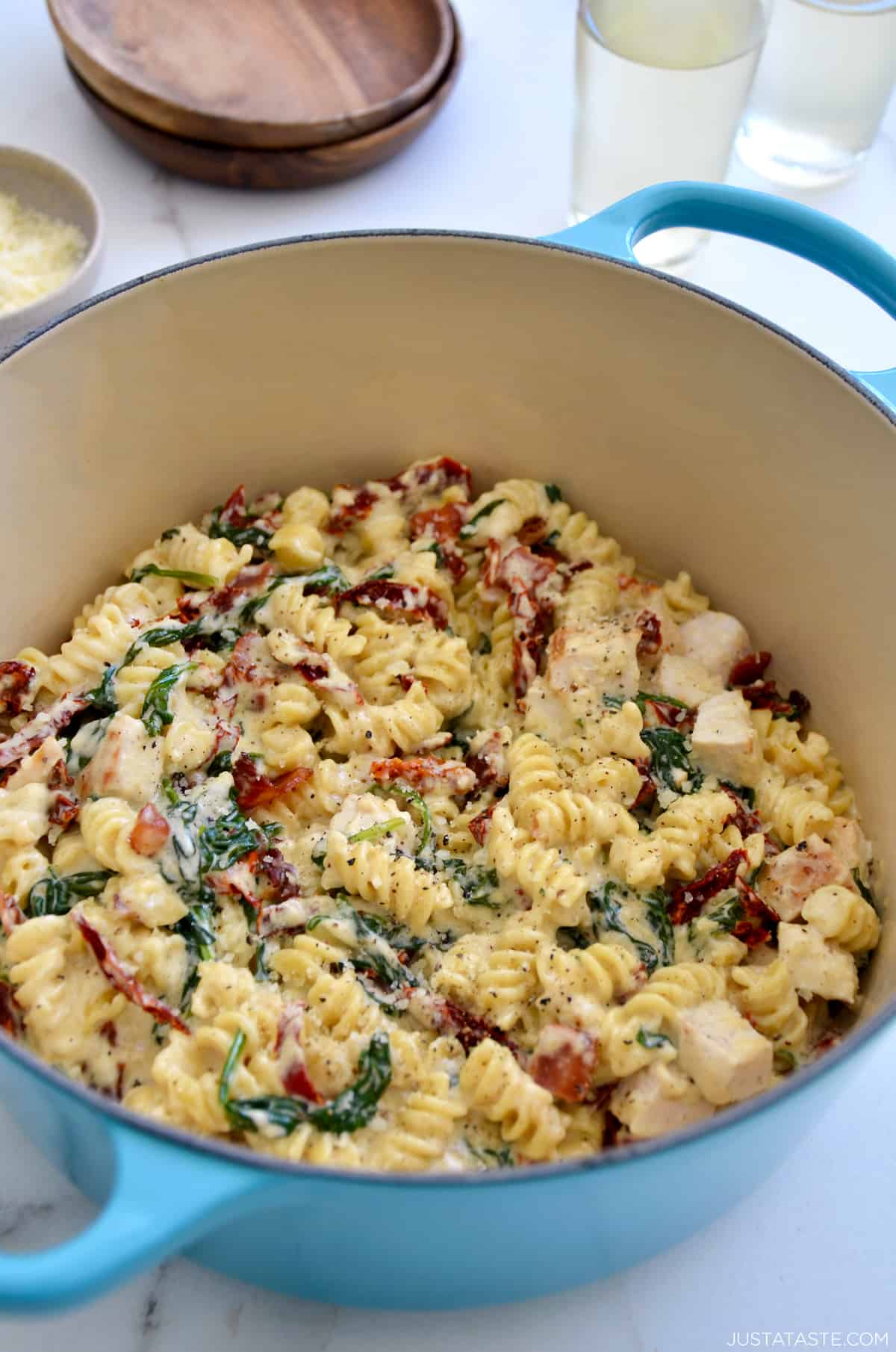 Creamy Tuscan pasta with diced chicken breasts, sun-dried tomatoes and spinach in a Dutch oven next to a small bowl containing Parmesan cheese.