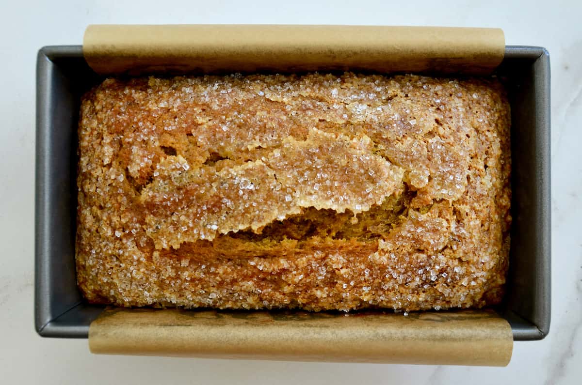 A loaf of pumpkin banana bread topped with sanding sugar in a parchment paper-lined loaf pan.