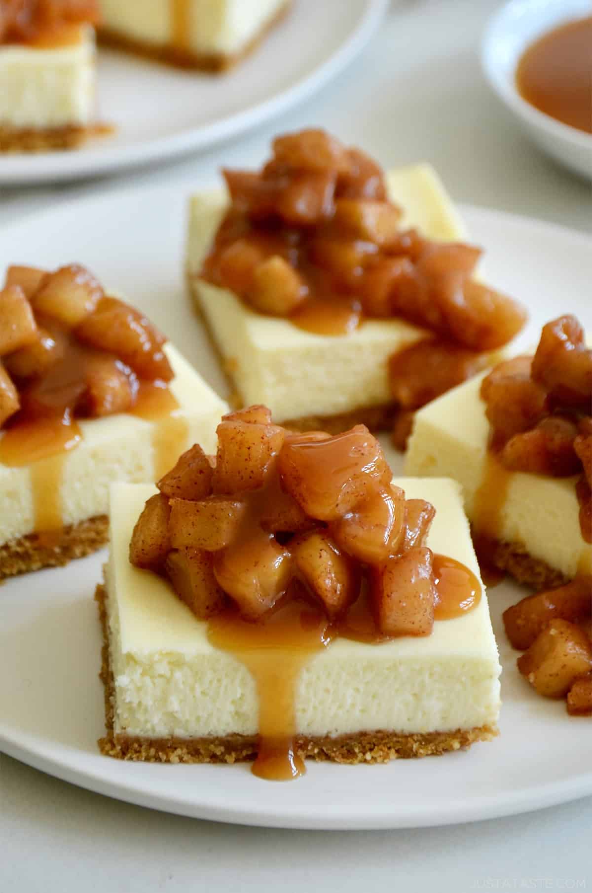 Four caramel apple cheesecake bars on a plate.