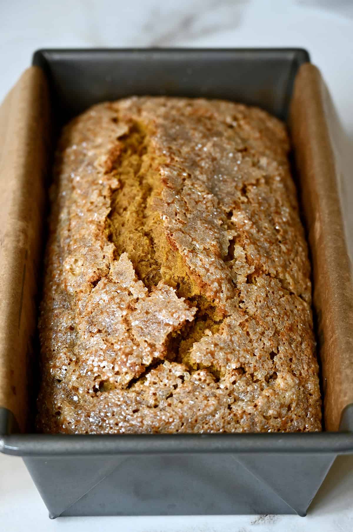 Baked pumpkin banana bread with a crackly sanding sugar topping in a loaf pan.