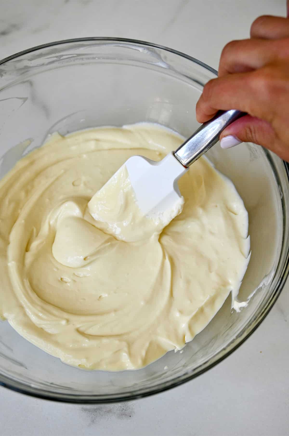 Creamy cheesecake filling in a mixing bowl with a spatula.