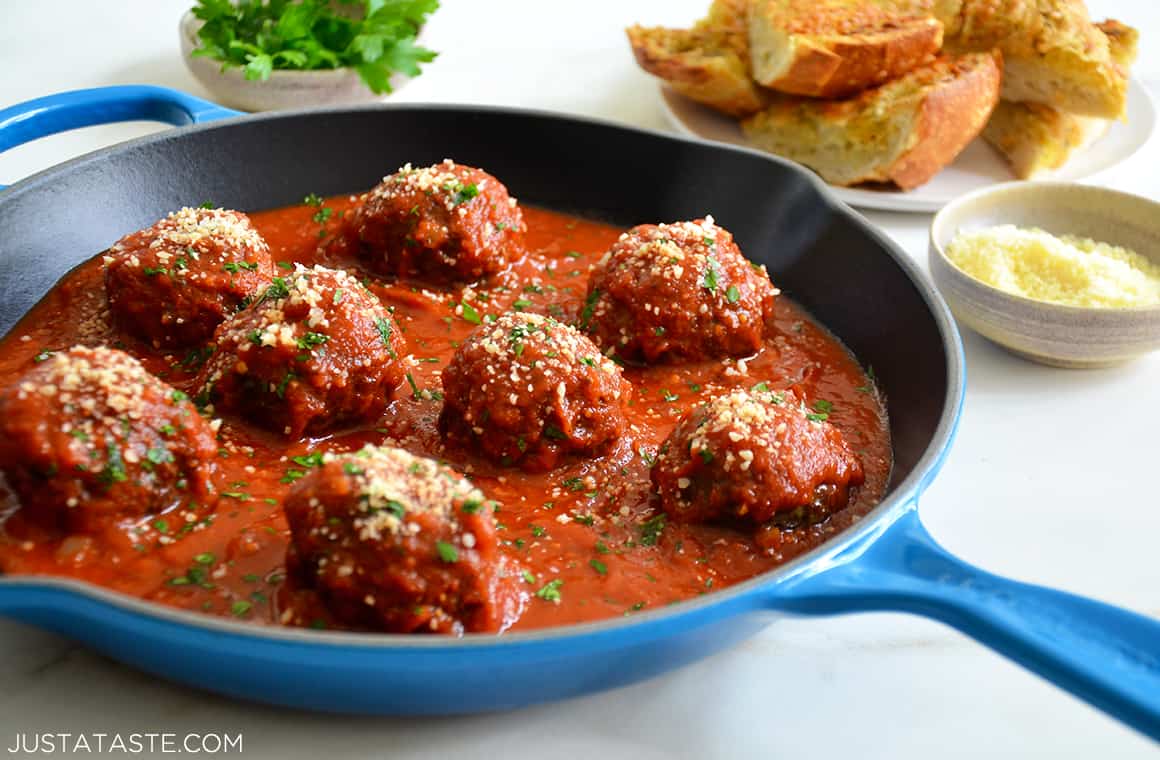 A skillet containing marinara sauce and Cheese-Stuffed Meatballs next to a plate with Garlic Dippers