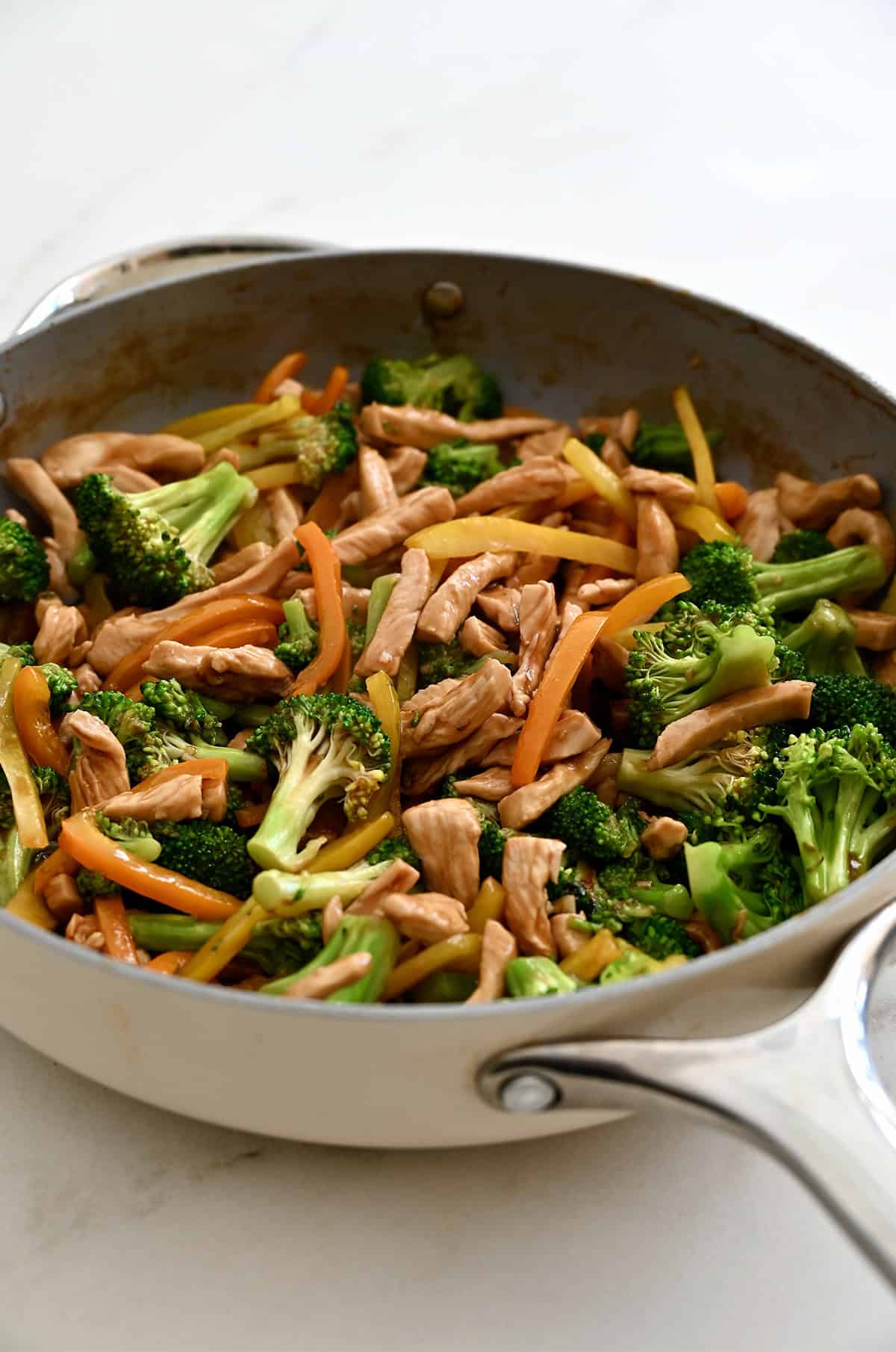 A large skillet containing chicken and veggie stir-fry in a savoy sauce.