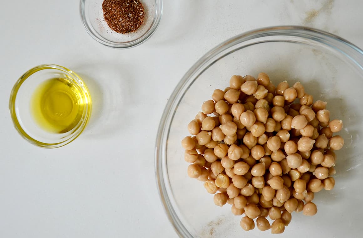A glass bowl containing chickpeas with seasonings and olive oil