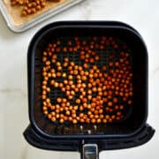 Crispy chickpeas on a parchment paper-lined baking sheet and also in an air fryer basket.