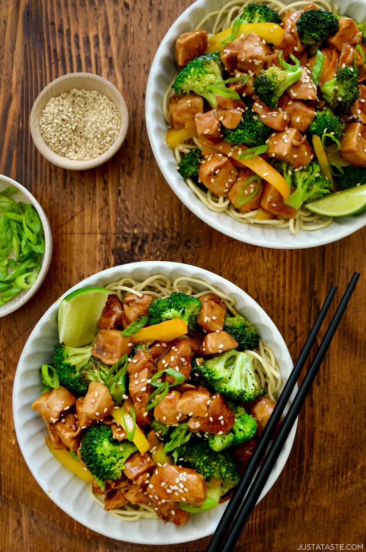 Bowls are filled with chicken and broccoli stir fry, with dishes of sesame seeds and scallions nearby.