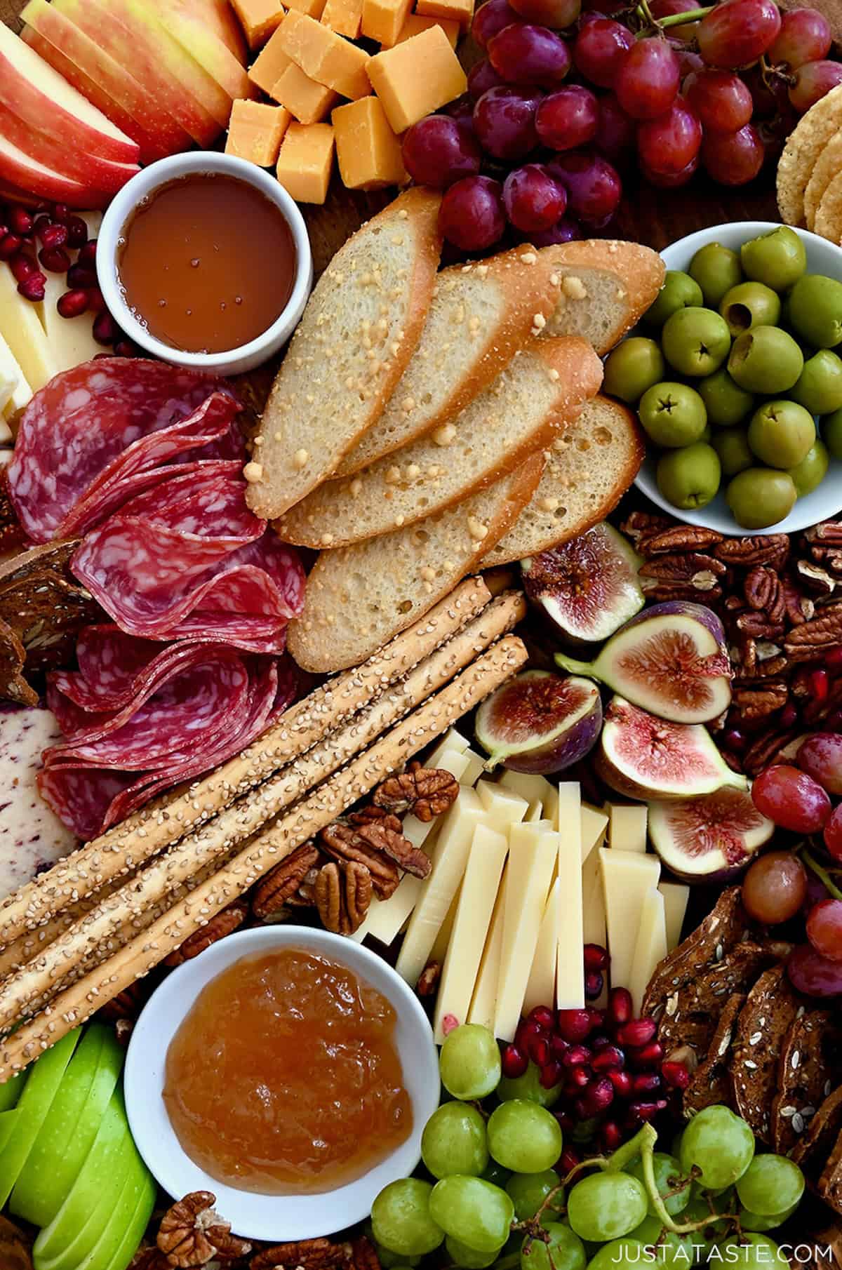 A closeup view of a fall-inspired meat and cheese board with figs, olives, grapes, pecans, salami, crackers and slices of cheese.
