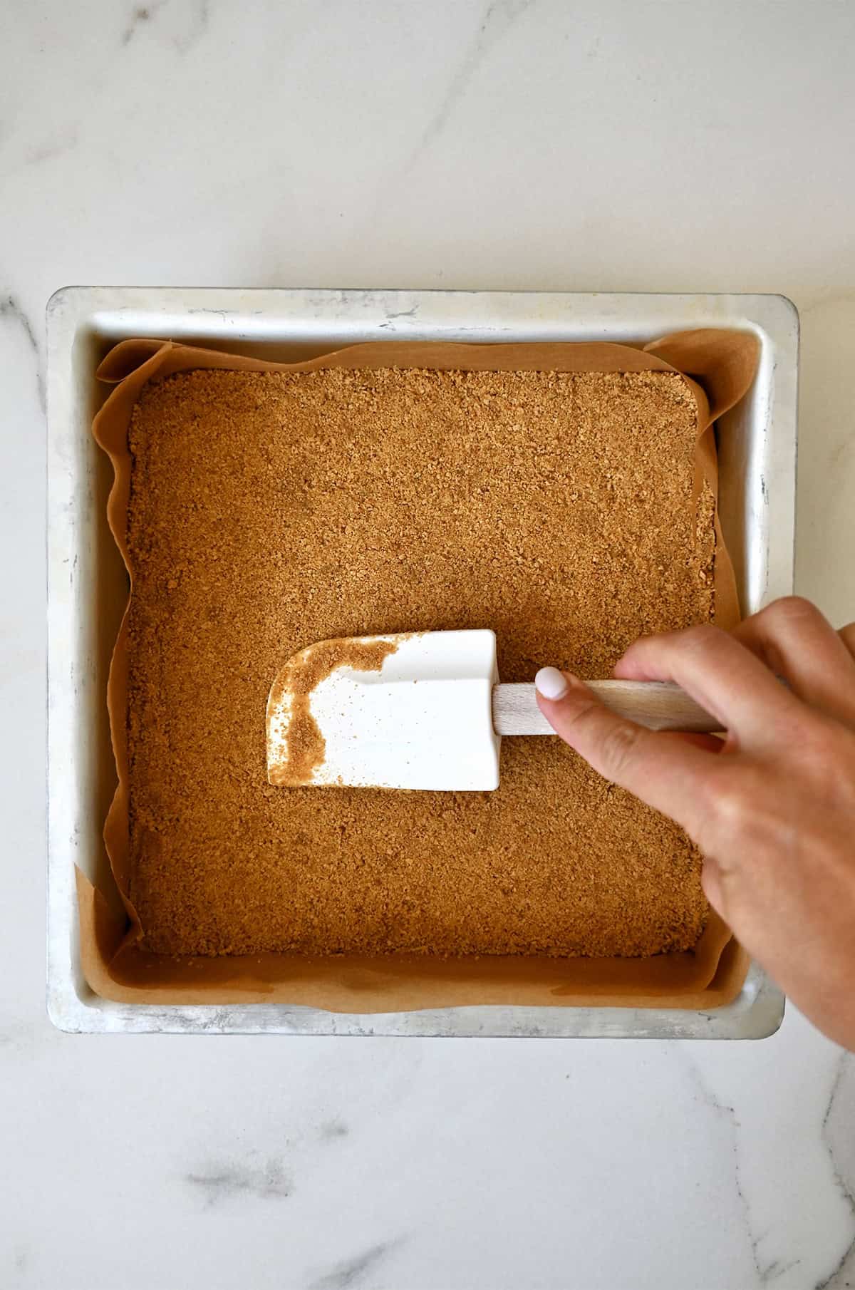Forming a graham cracker crust in an 8-inch square baking dish lined with parchment paper.
