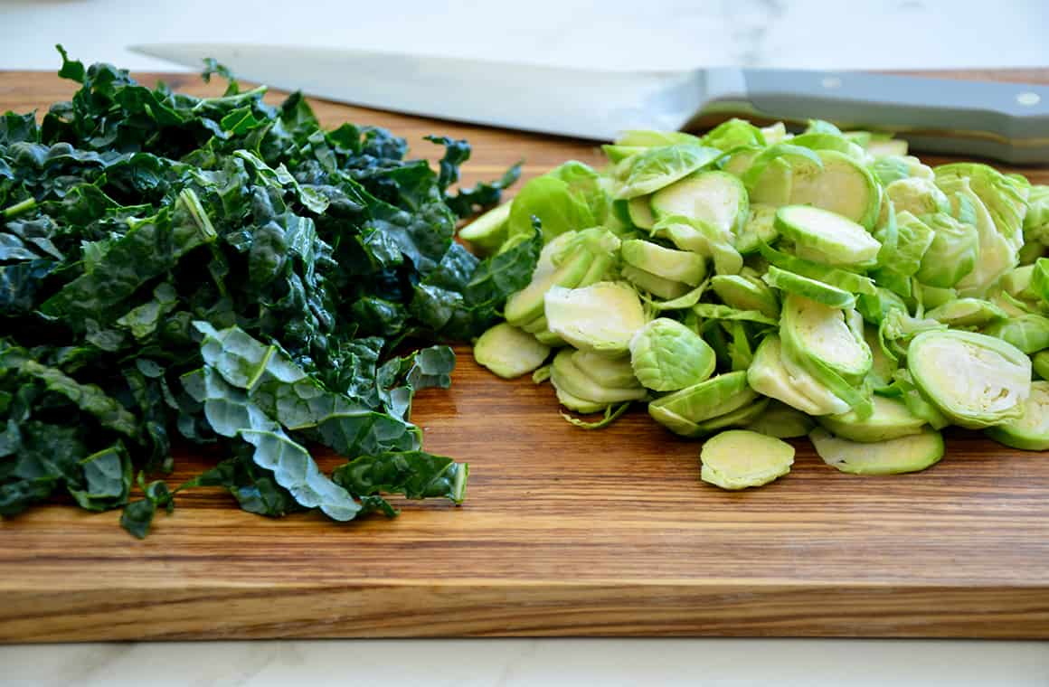 Chopped kale and Brussels sprouts on a cutting board with a knife