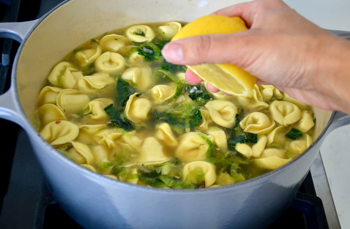 A hand holding a lemon squeezing lemon juice into a large pot of soup 