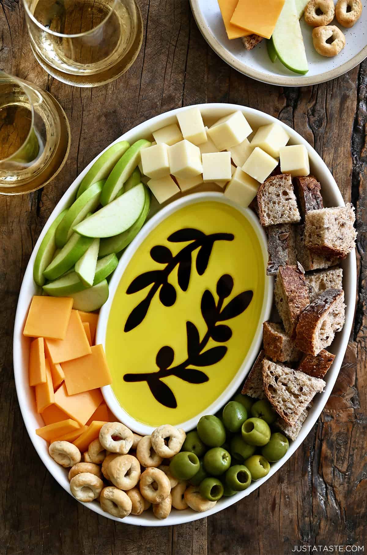 Olive branch olive oil and balsamic vinegar charcuterie board with apple slices, cheese cubes, olives and chunks of bread.