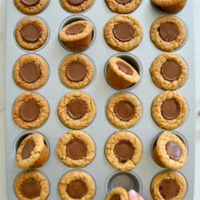 A child's hand reaching for a Mini Peanut Butter Cup Cookie in a muffin tin