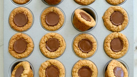 A child's hand reaching for a Mini Peanut Butter Cup Cookie in a muffin tin