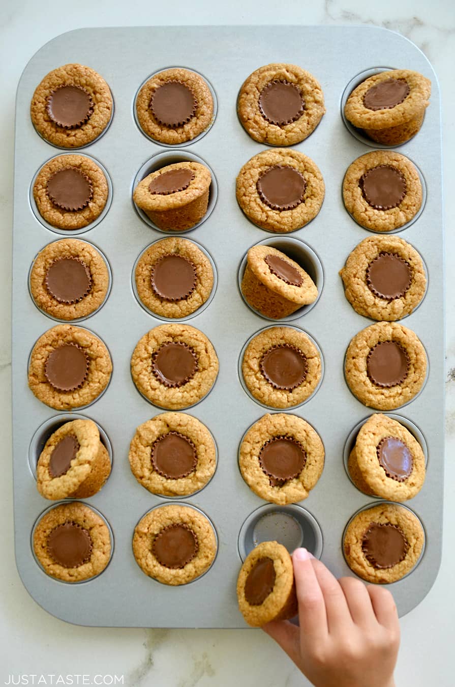 A child's hand reaching for a Mini Peanut Butter Cup Cookie in a muffin tin