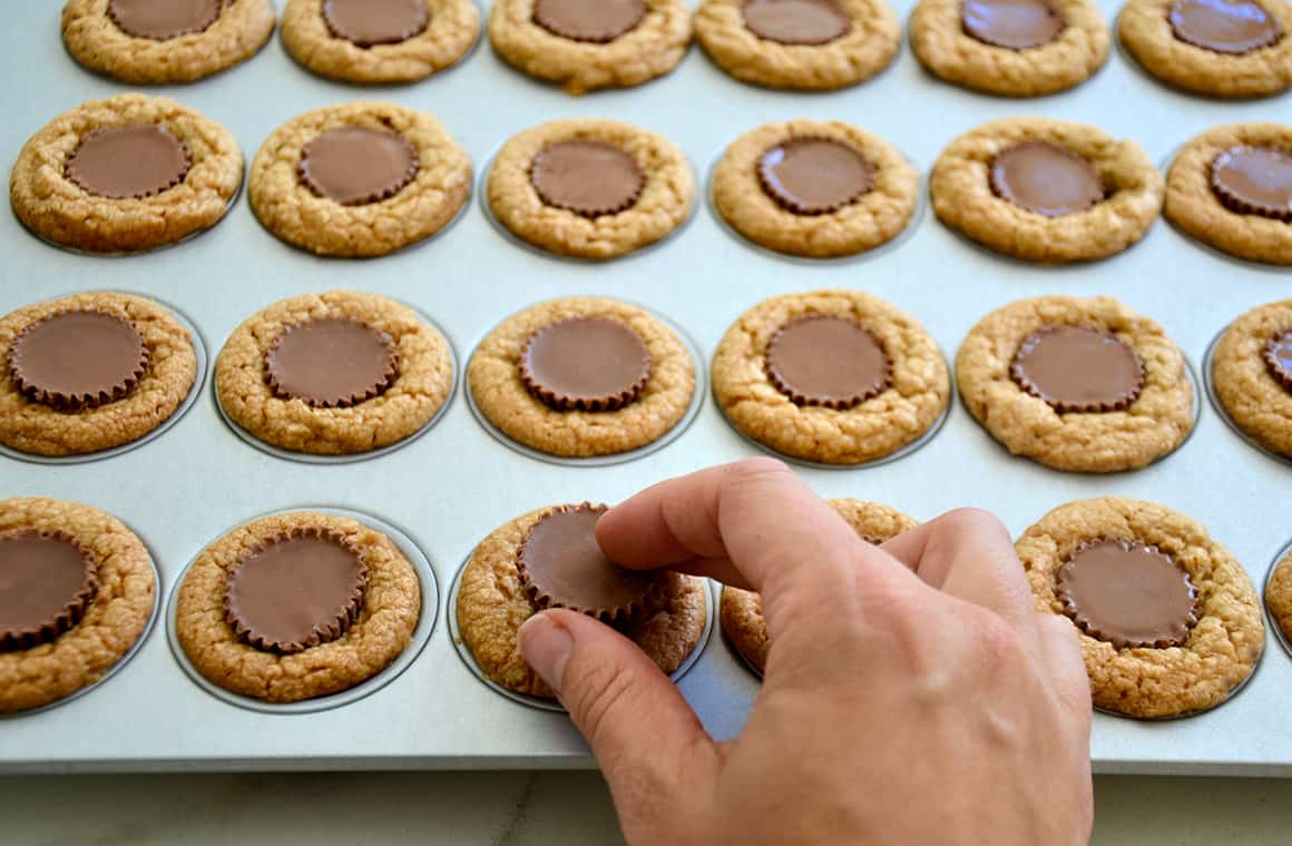 A hand placing a peanut butter cup into the center of a warm cookie