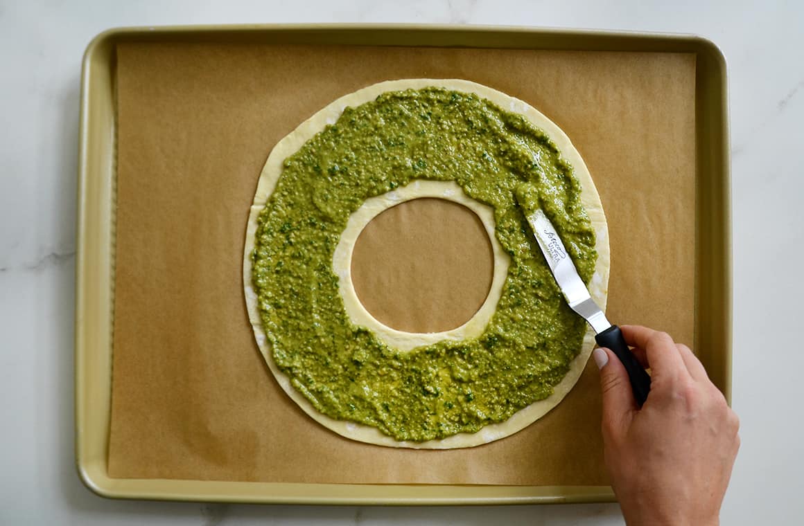 Pesto being spread atop pastry with an offset spatula