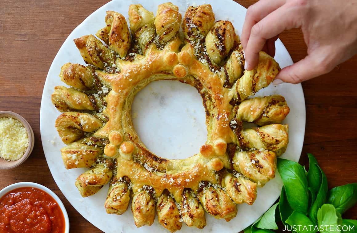 A hand reaching for a piece of easy Pesto Puff Pastry Wreath 