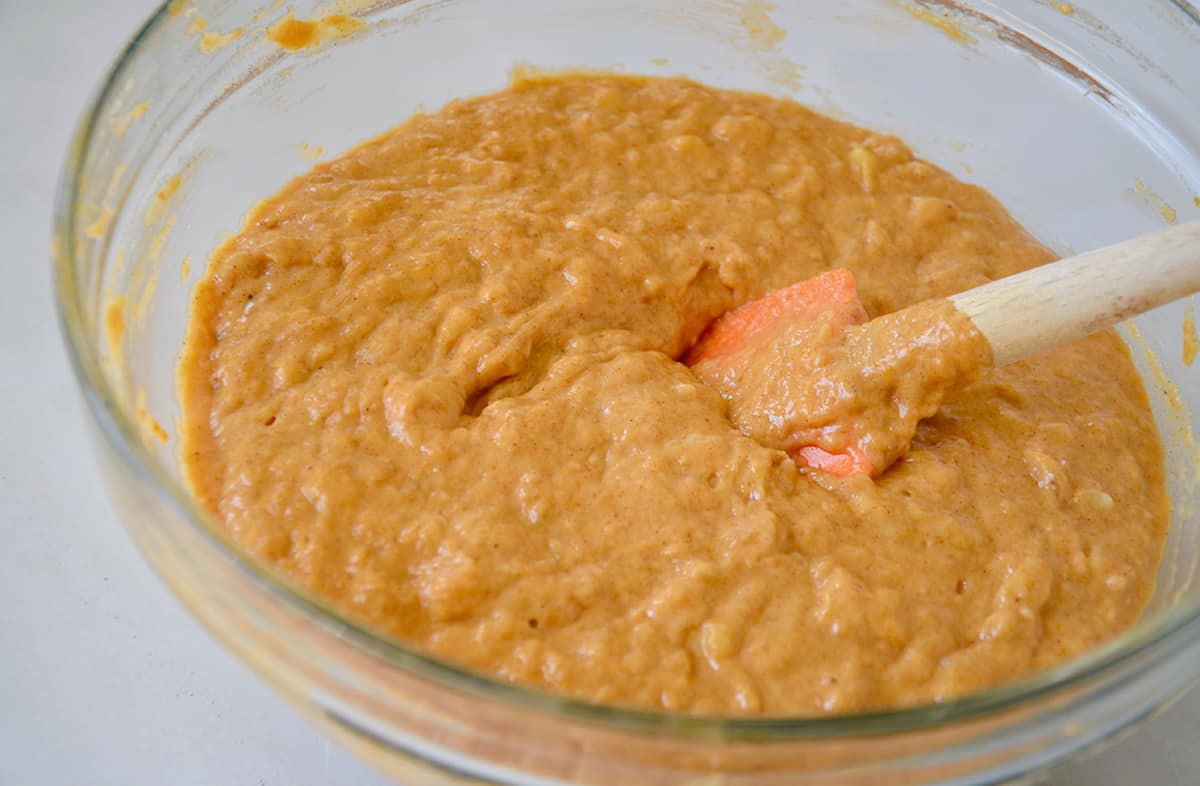 Pumpkin banana bread batter is in a glass bowl, being stirred with a spatula.