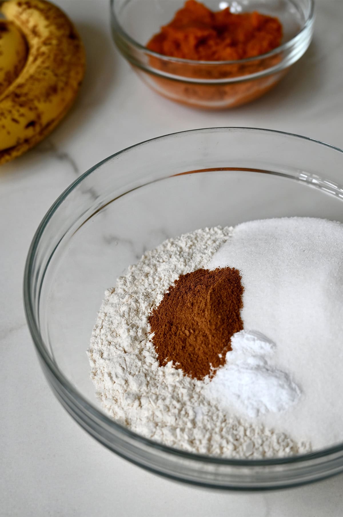 Dry ingredients for banana pumpkin bread in a glass bowl.
