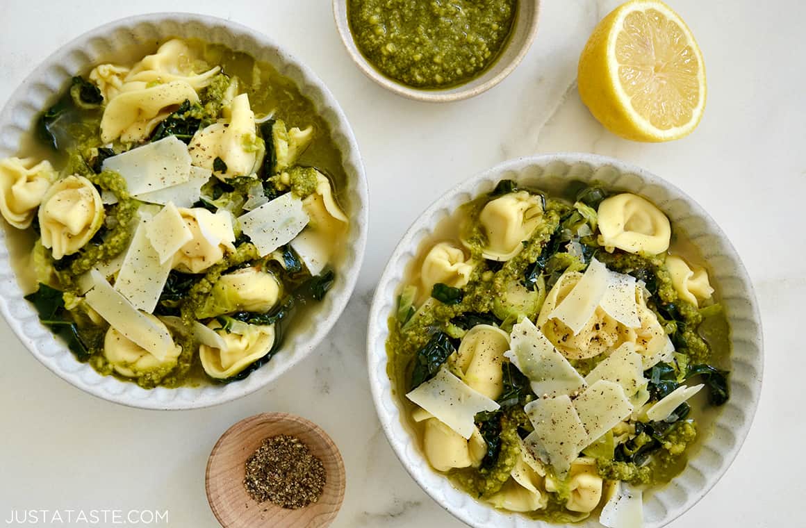 Two bowls containing Quick Tortellini Soup with Greens topped with pesto and shaved Parmesan cheese