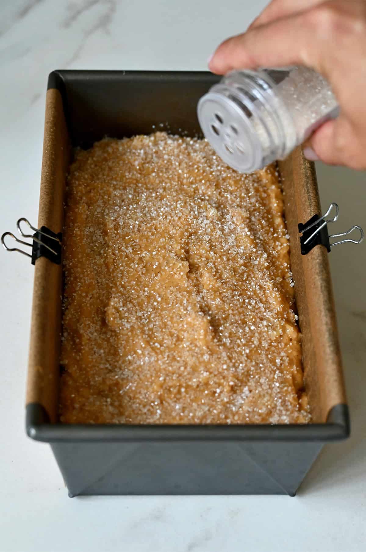 Sprinkling sanding sugar atop pumpkin banana bread batter in a loaf pan before baking.