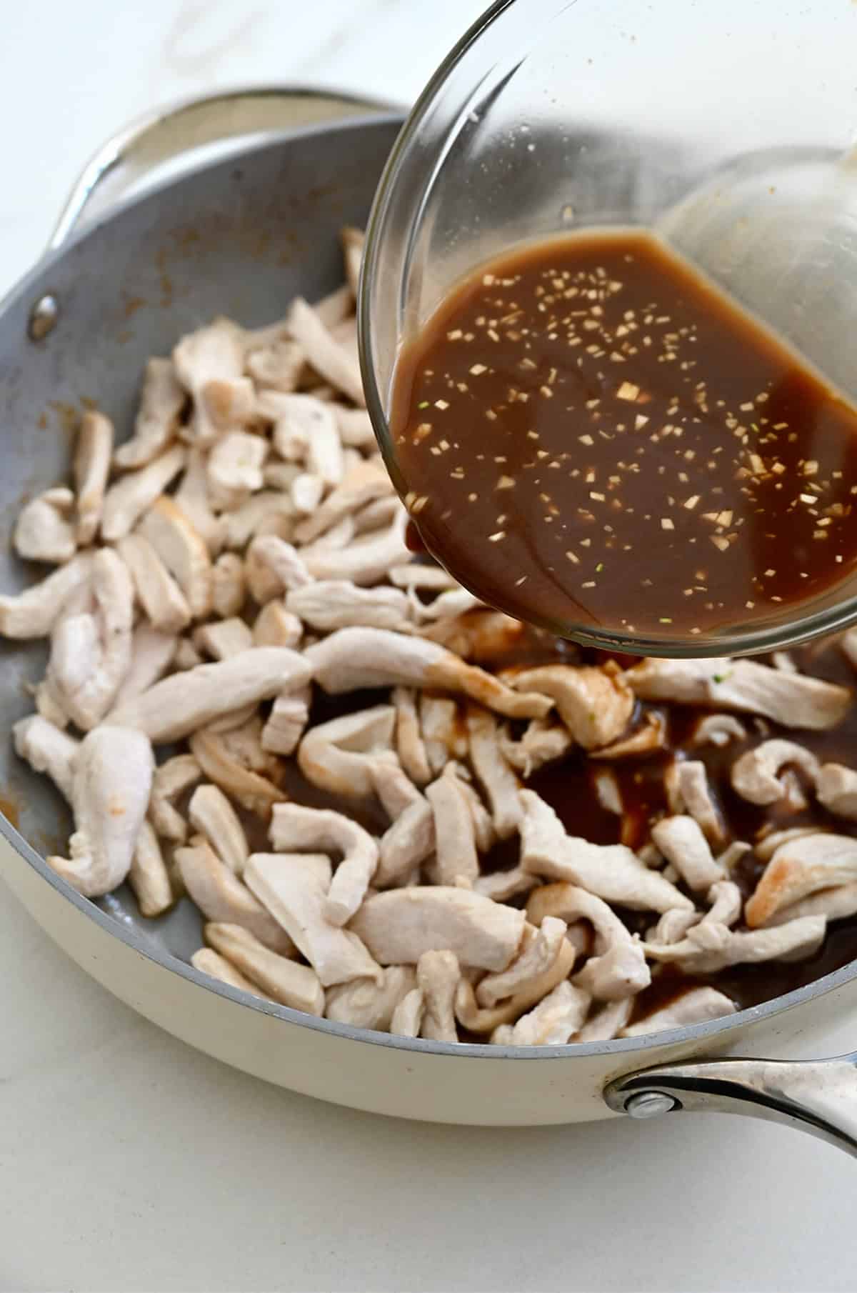 Adding stir-fry sauce to a large skillet with cooked chicken.