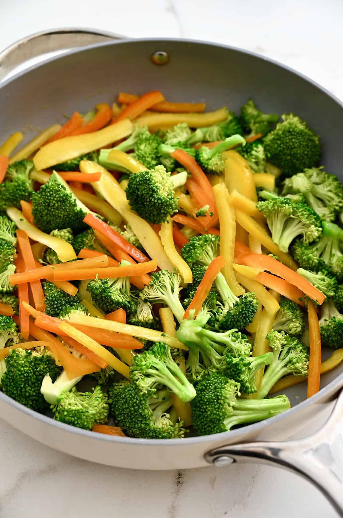 Stir-fried broccoli florets and sliced yellow and orange bell peppers in a large skillet.