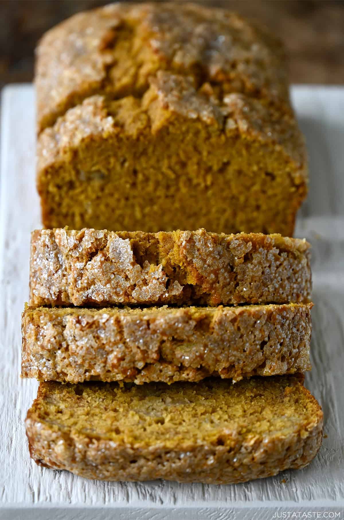 Thick slices of pumpkin banana bread with a golden crust and crackly sugar topping on a white serving board.