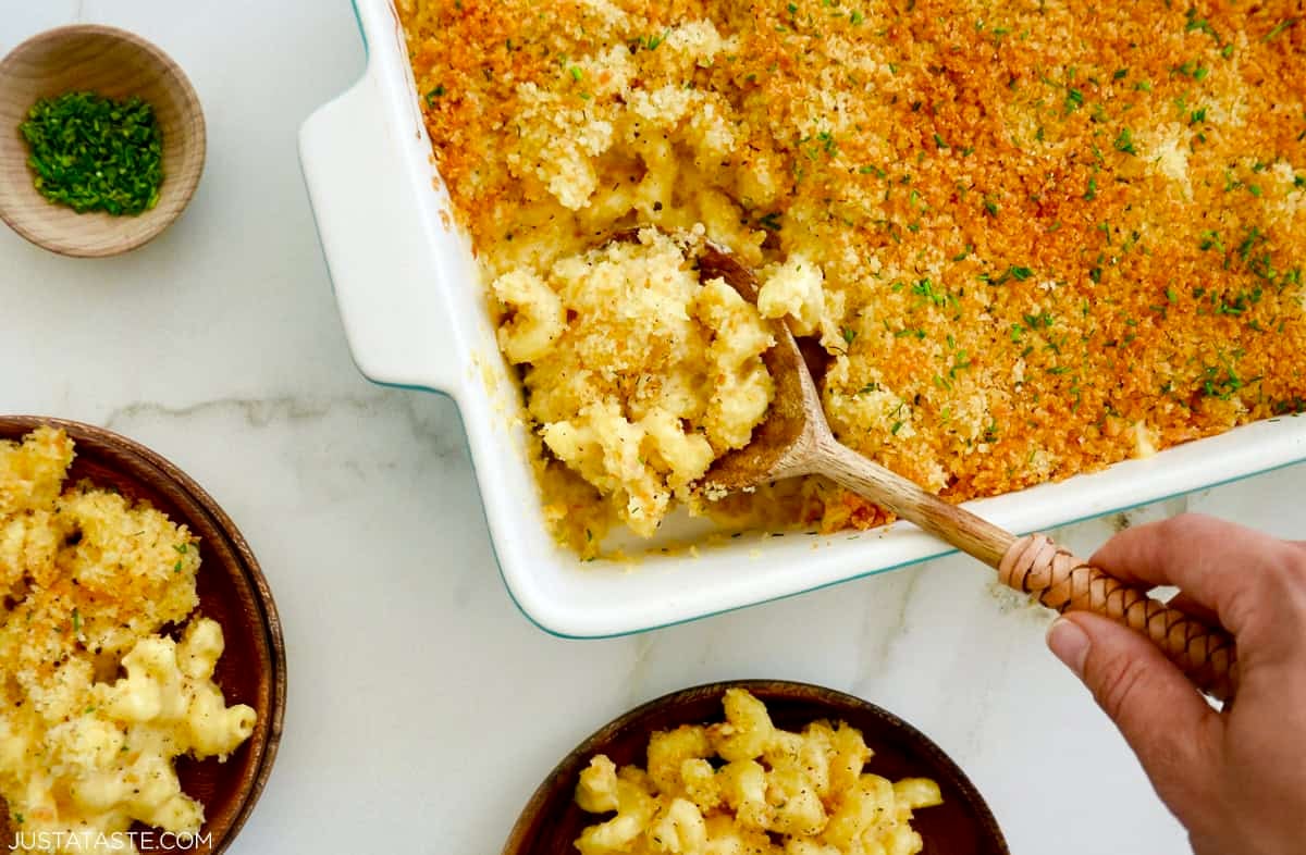 Homemade baked mac and cheese with roasted garlic and golden breadcrumb topping being scooped from a casserole dish.