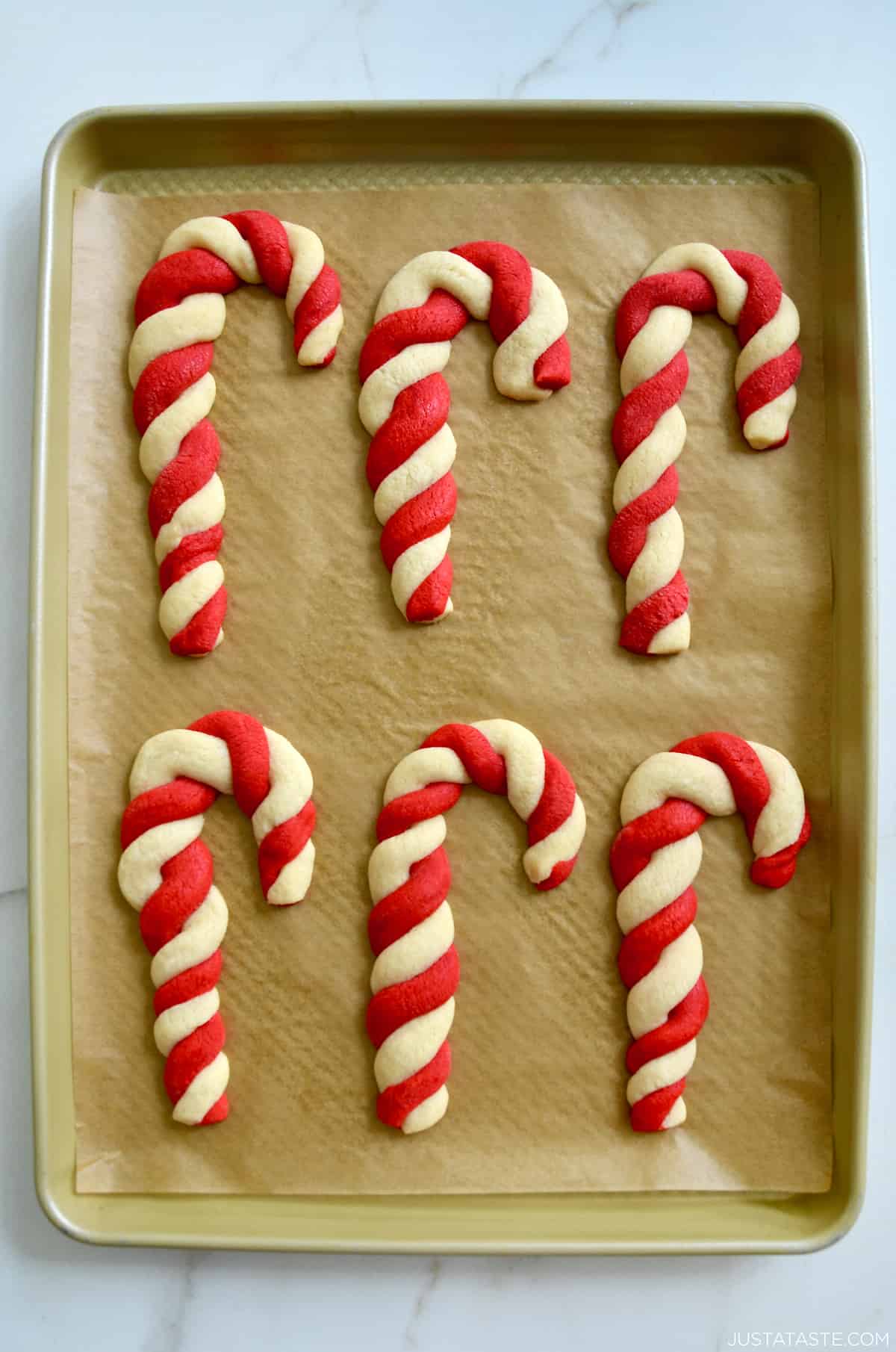 Freshly baked candy cane cookies on a parchment paper-lined baking sheet.